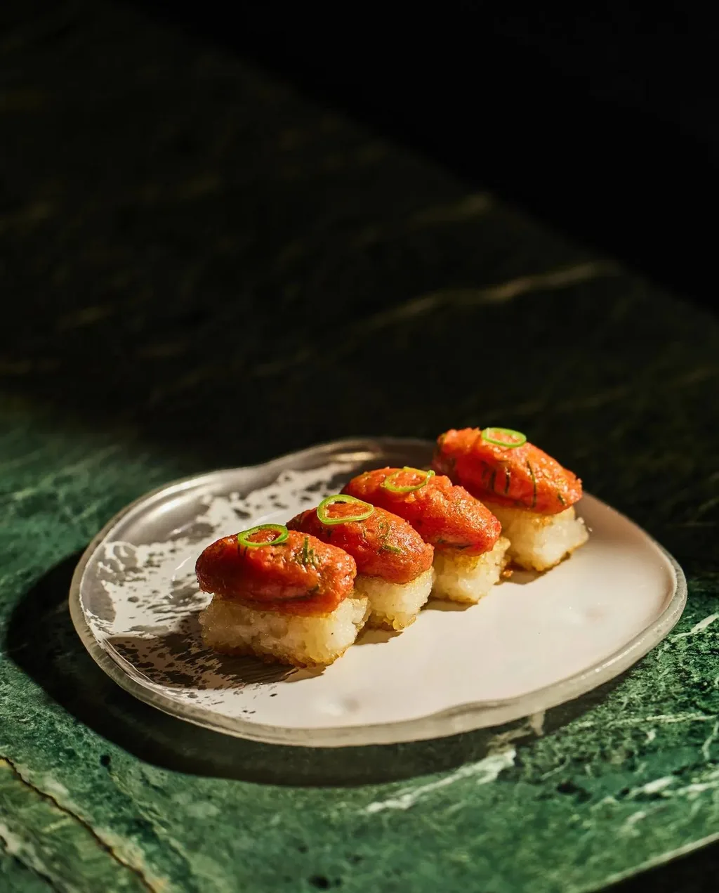 Seared salmon nigiri with green chile garnish on a ceramic plate