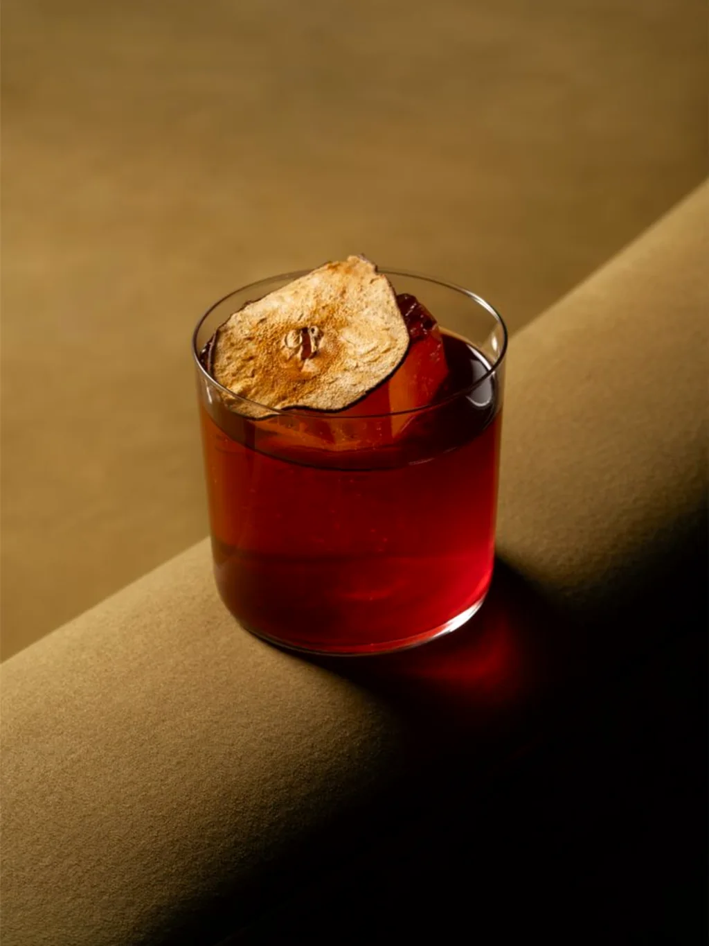 Red cocktail with a dried fruit garnish in a warm, intimate setting