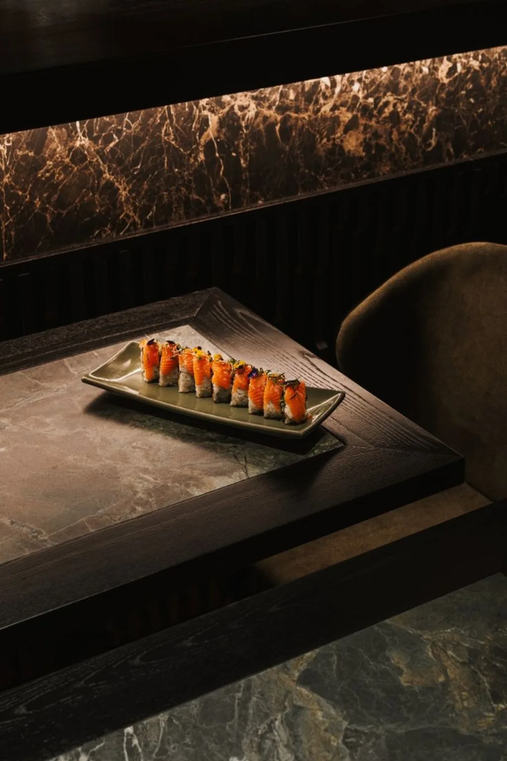 Salmon nigiri arranged on a dark plate in a warmly lit dining setting