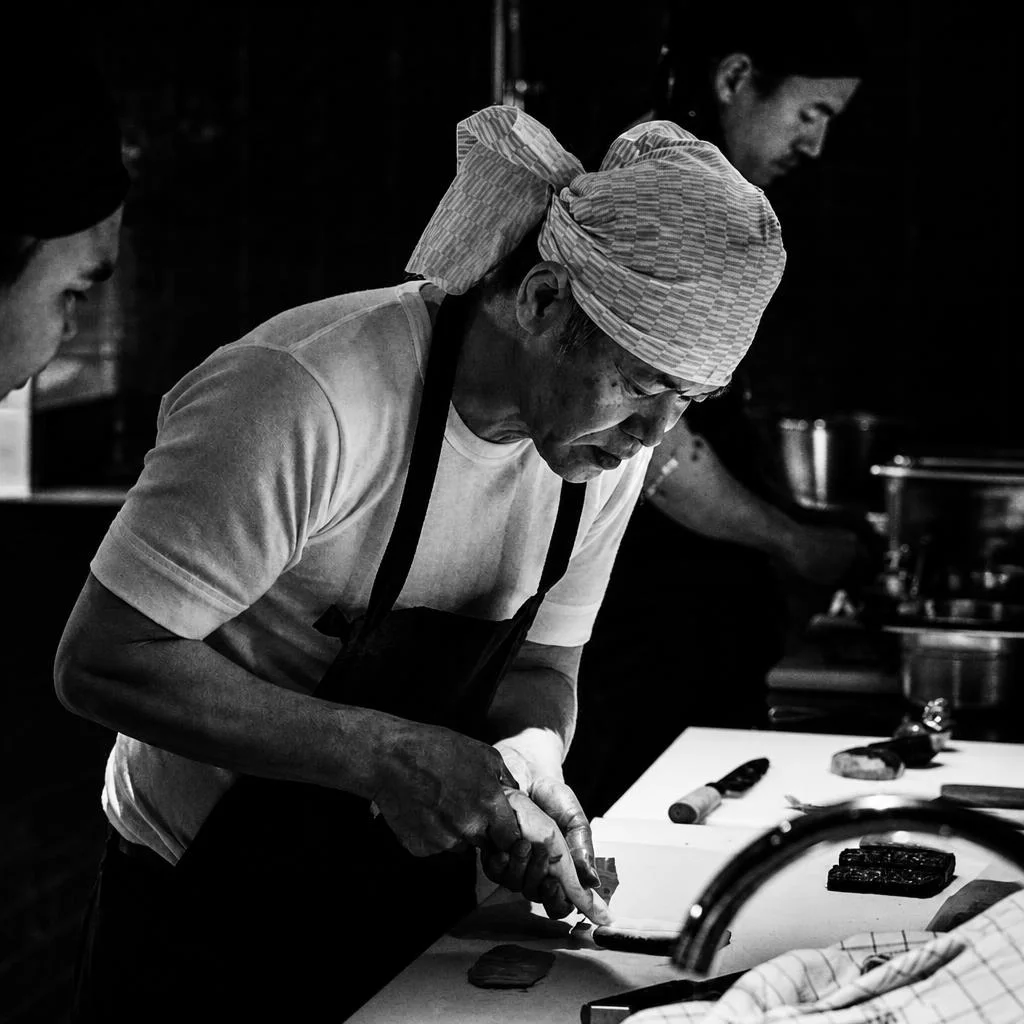 Chef preparing fish at a sushi counter in a high-contrast black-and-white photograph