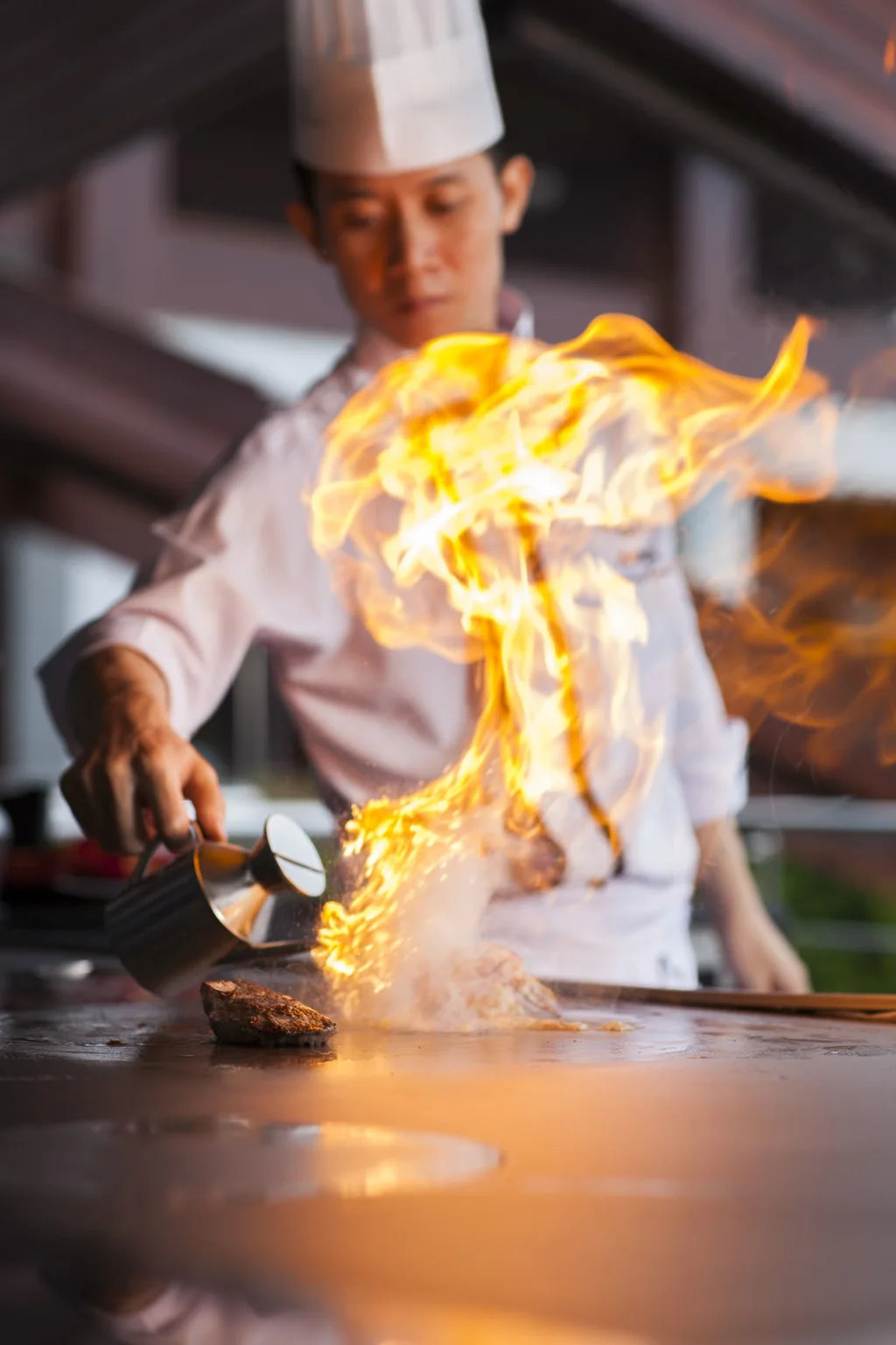 Chef searing steak on a teppanyaki grill as flames rise across the cooking surface